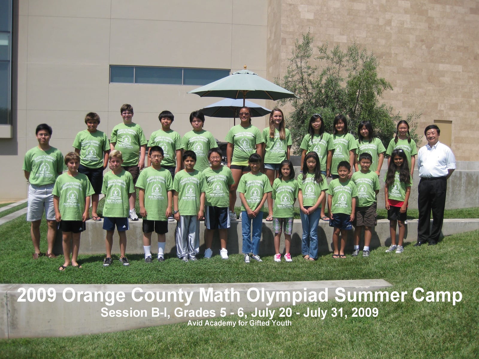 Twenty-four students in green Math Olympiad t-shirts stand in two rows outdoors, with Dr. Li at the right edge. A printed caption bar names the 2009 Orange County Math Olympiad Summer Camp and Avid Academy for Gifted Youth.