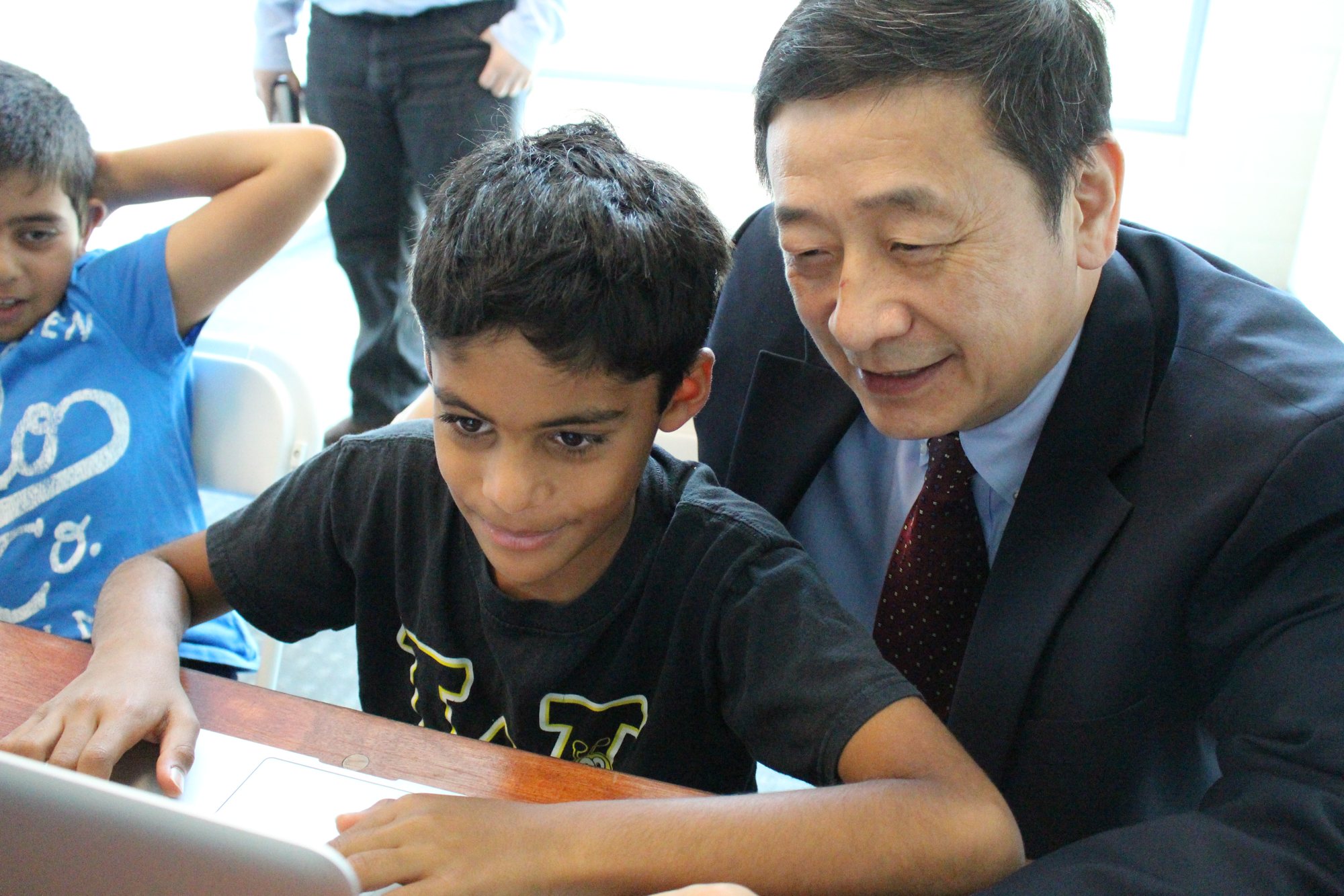 Dr. Li leans in beside a student working on a laptop in class.