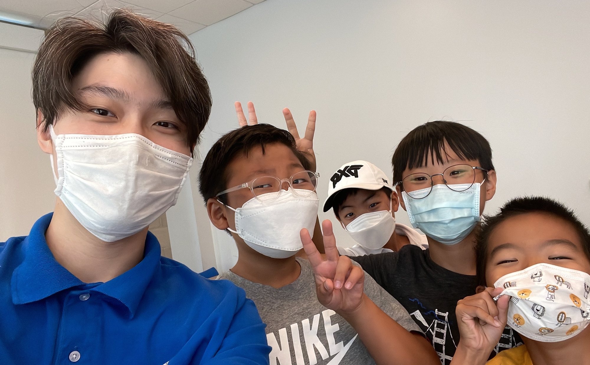 Five students in face masks crowd into a selfie, two making peace signs.