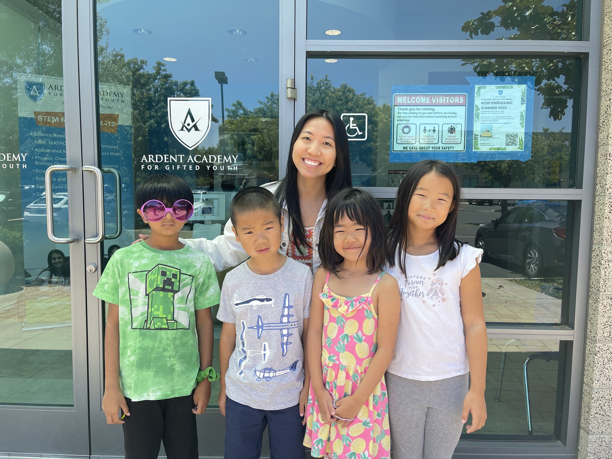 An instructor and four young students, one in novelty glasses, stand at the Ardent Academy front doors.