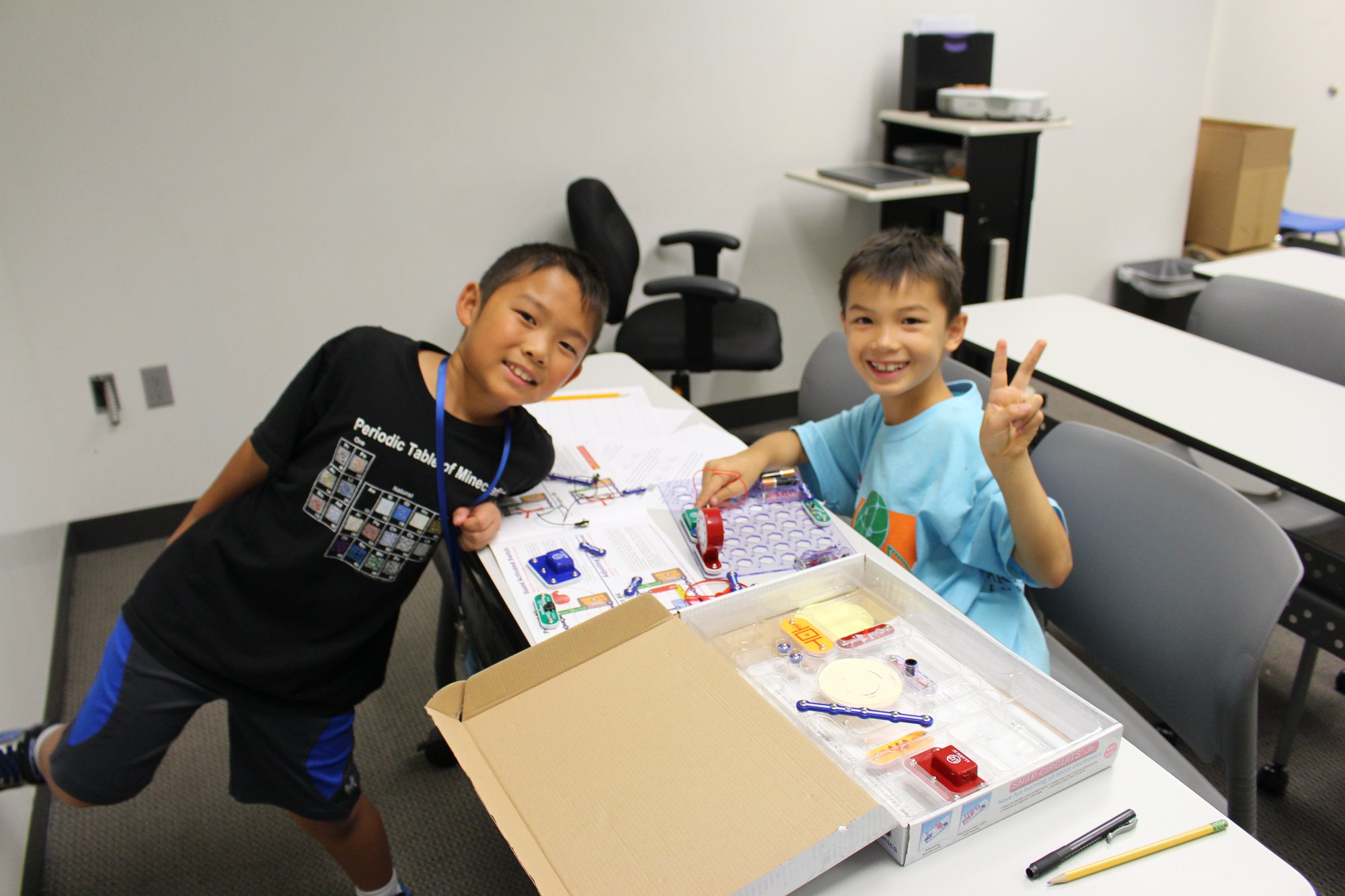 Two boys pose at a classroom table with a building kit.