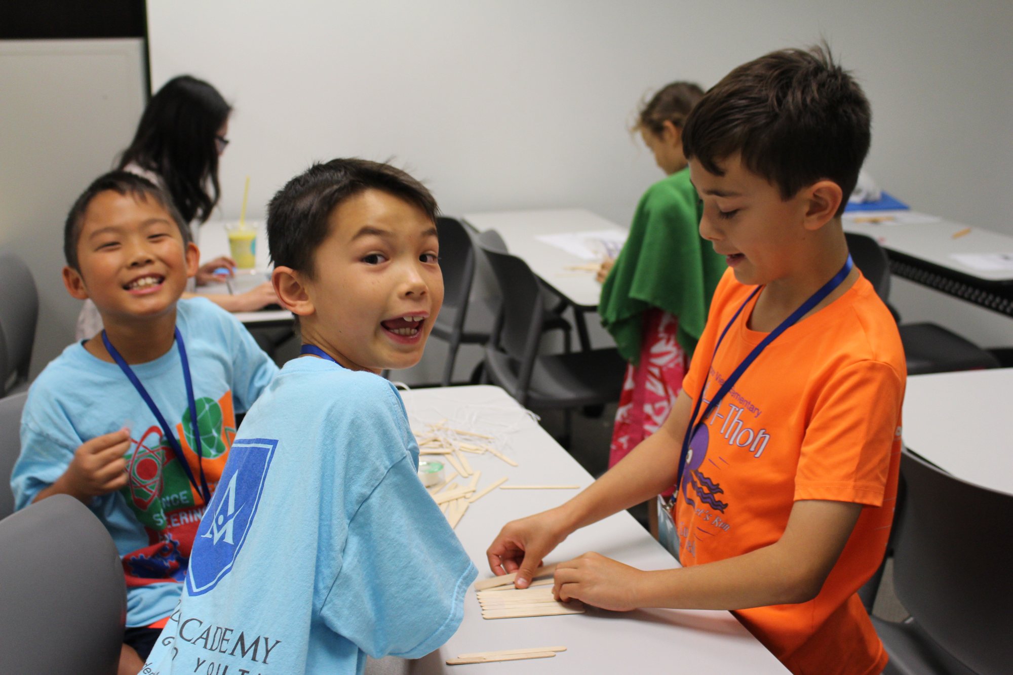 Students in Ardent Academy T-shirts build a project together at a classroom table.