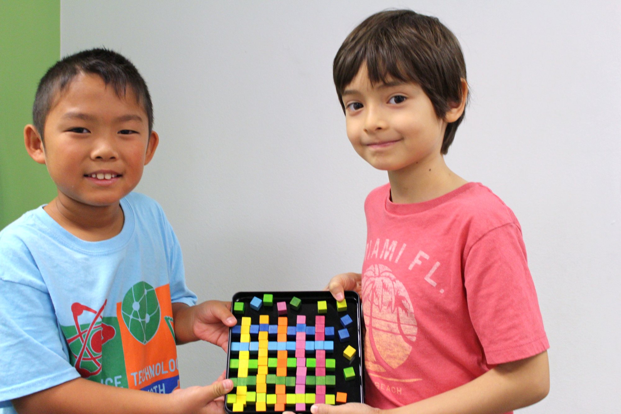 Two boys hold up a colourful woven square they made.