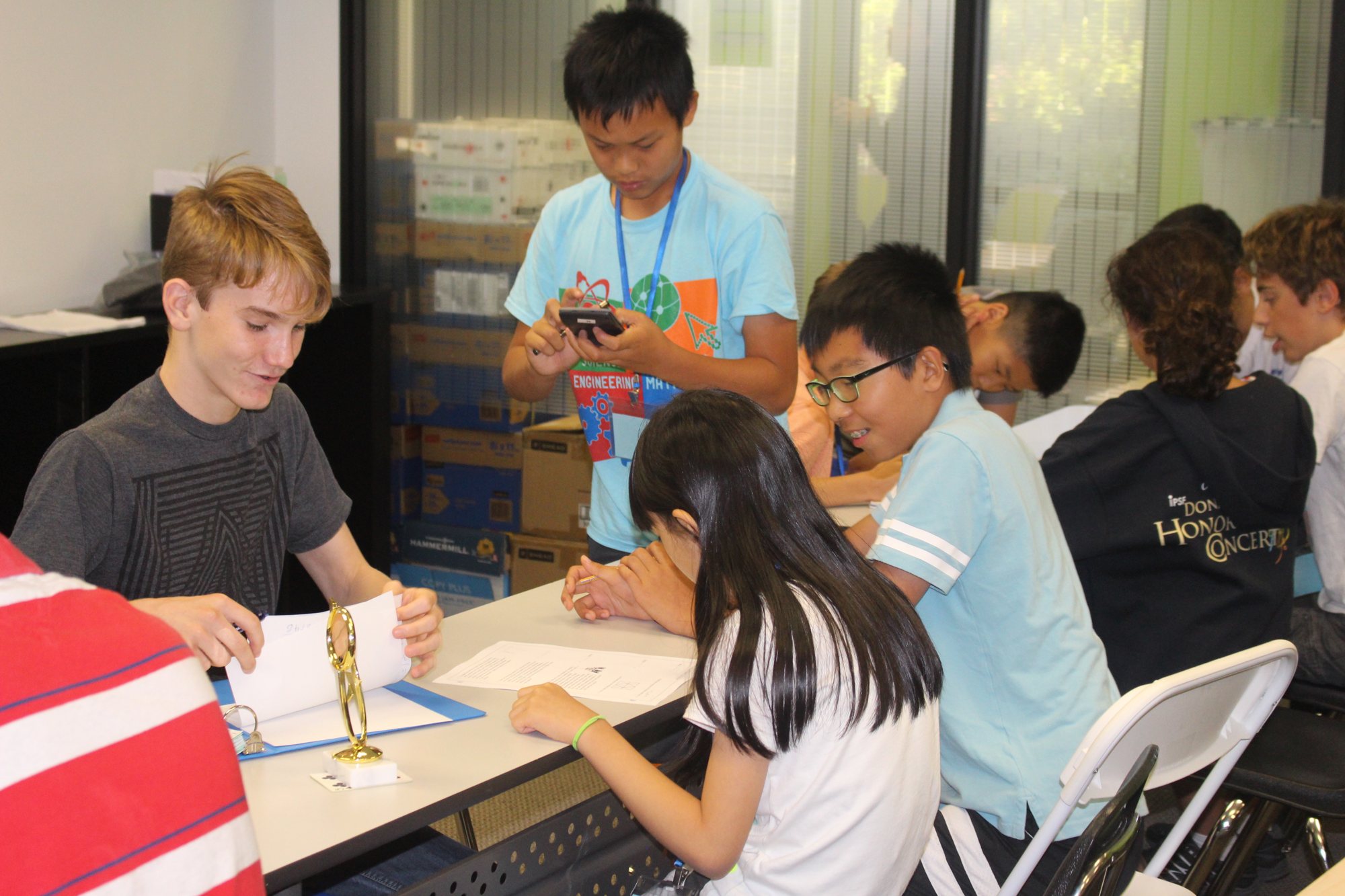 Students work together around tables in a busy classroom.